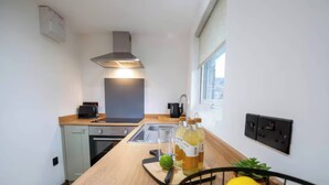 A modern kitchen with a wooden countertop, stainless steel appliances, a built-in oven, and a range hood. There is a window providing natural light and a black electrical outlet on the wall. - Fir Cottages (Llanrwst)