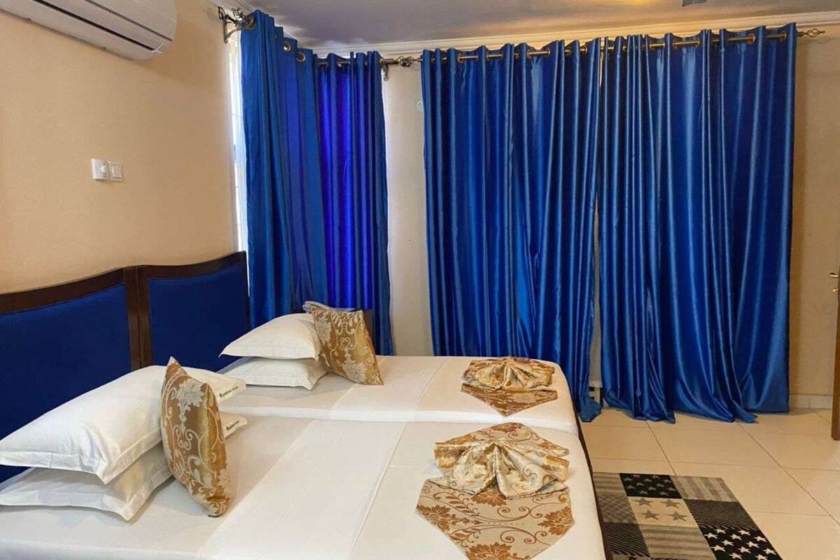 A hotel room with two beds, blue curtains, and a patterned rug.