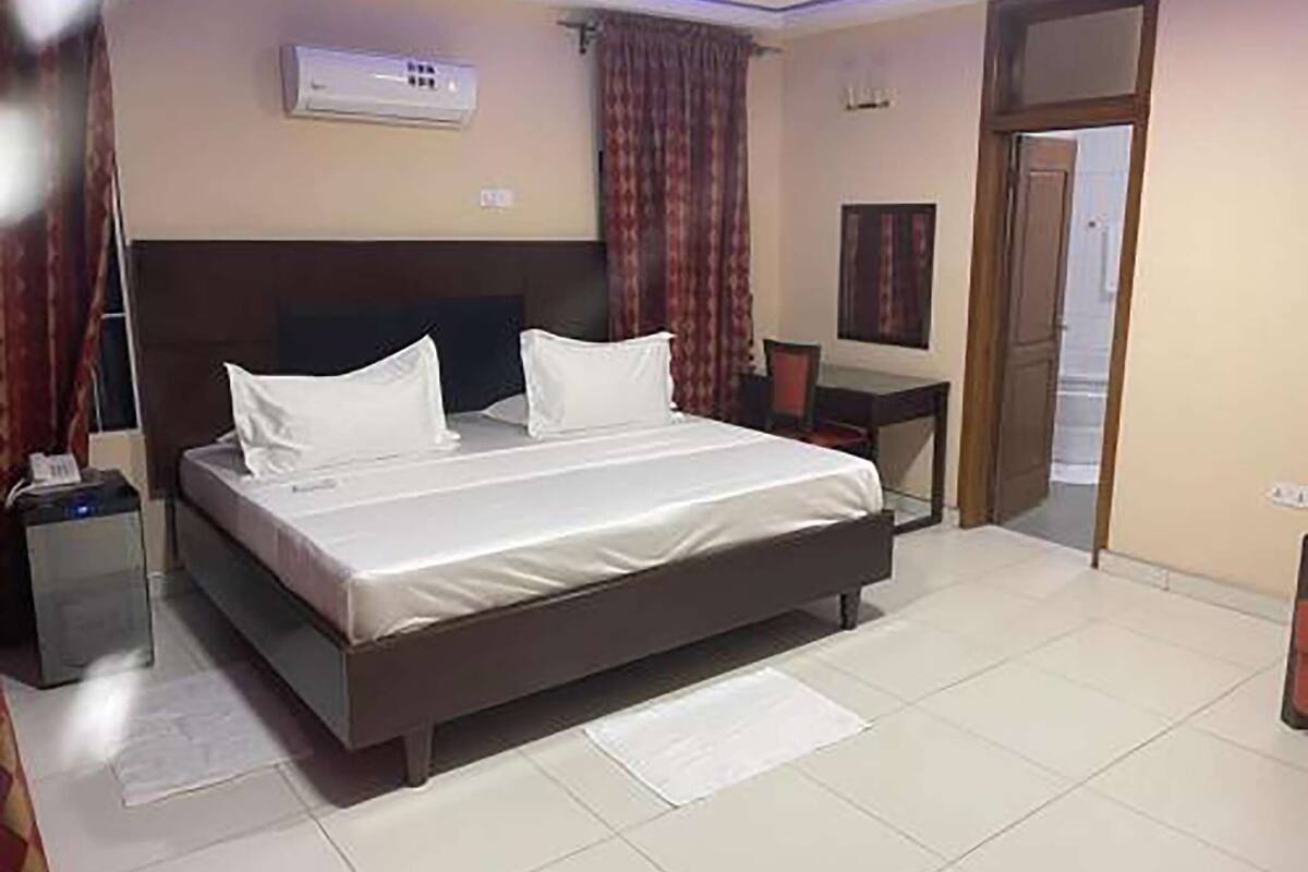 A hotel room with a bed, a desk, and an air conditioning unit.