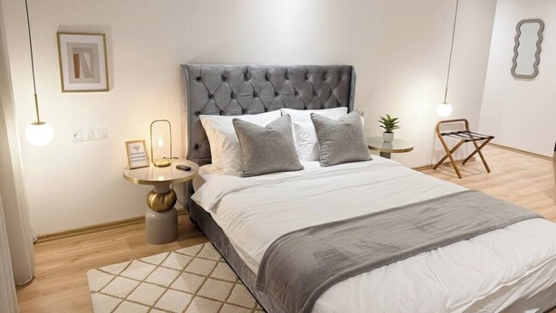 A modern bedroom with a tufted headboard, a round bedside table, a small potted plant, and a hanging light fixture. - Luxurious 2-bedroom Apartment in Heart of Rabat (Rabat)