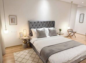 Ein modernes Schlafzimmer mit einer gepolsterten Kopfteile, einem runden Nachttisch, einer kleinen Topfpflanze und einer Pendelleuchte.
