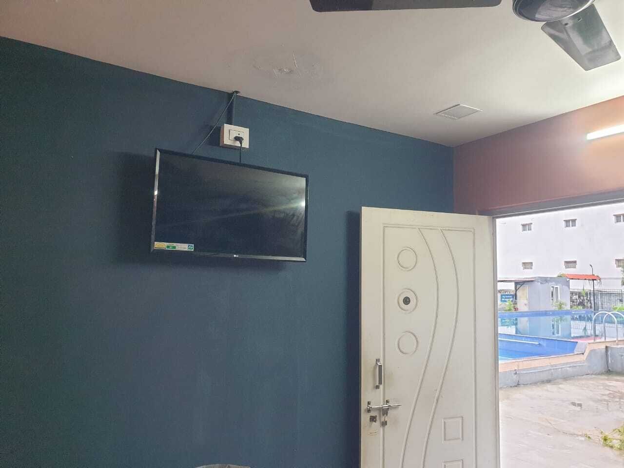A room with a flat-screen TV mounted on the wall, a white door with circular handles, and a view of an outdoor swimming pool.