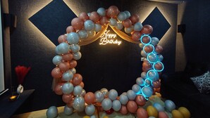 Une pièce décorée d’une arche de ballons et d’un panneau néon sur lequel on peut lire « Joyeux anniversaire ».