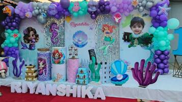 Un espacio para eventos decorado, con un escenario que incluye un cartel con un nombre, globos y adornos temáticos.