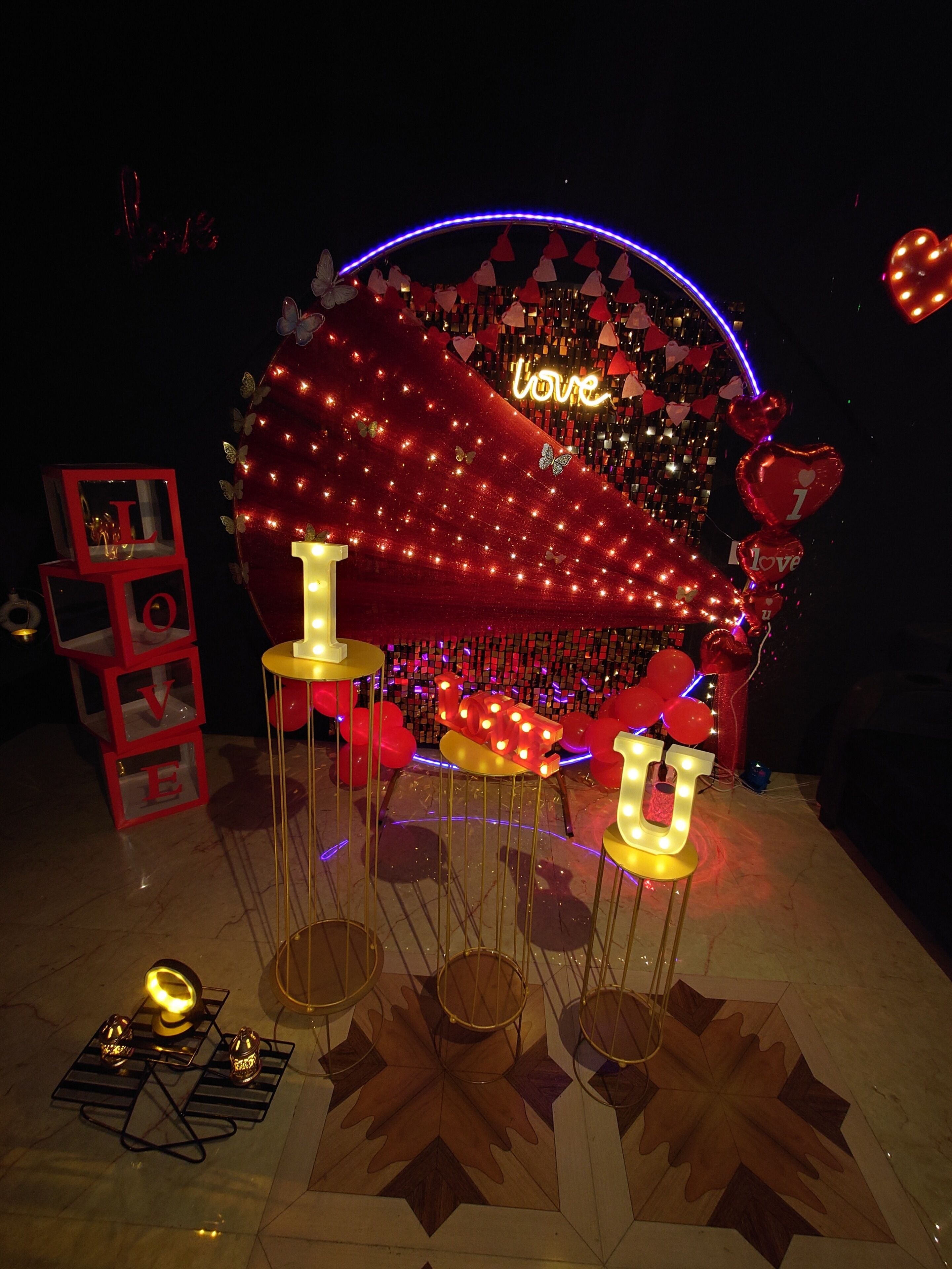 A decorative setup with a heart-shaped backdrop, illuminated letters spelling 'love,' and a series of red balloons.