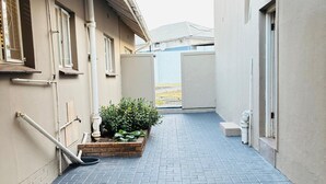 A narrow paved pathway leading to a building entrance, with a covered area overhead and a small planter with greenery. - Cozy stays 30km from ORTambo within 10km to restaurants, malls and Goldreef cty (Alberton)