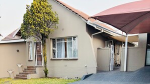 A residential house with a paved driveway, a small garden with gravel and plants, and a tree with yellow flowers.