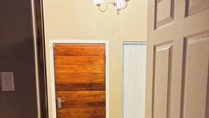 A hallway with a wooden door, a white door, and a light fixture above.