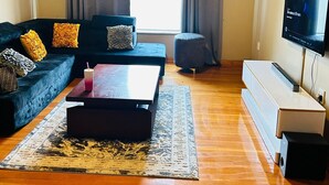 A living room with a dark-colored sofa, a wooden coffee table, a TV, and a large window with curtains.