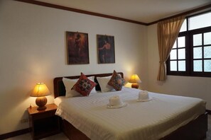 Una habitación de hotel con una cama grande, dos cuadros en la pared, dos lámparas de noche y una ventana con cortinas.