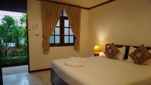 Camera d'albergo con un letto, una finestra con tende e una lampada da comodino, con vista su piante.