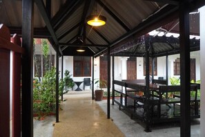A covered outdoor area with a wooden table and chairs, a concrete floor, and potted plants. - Residy Downtown (Patong)