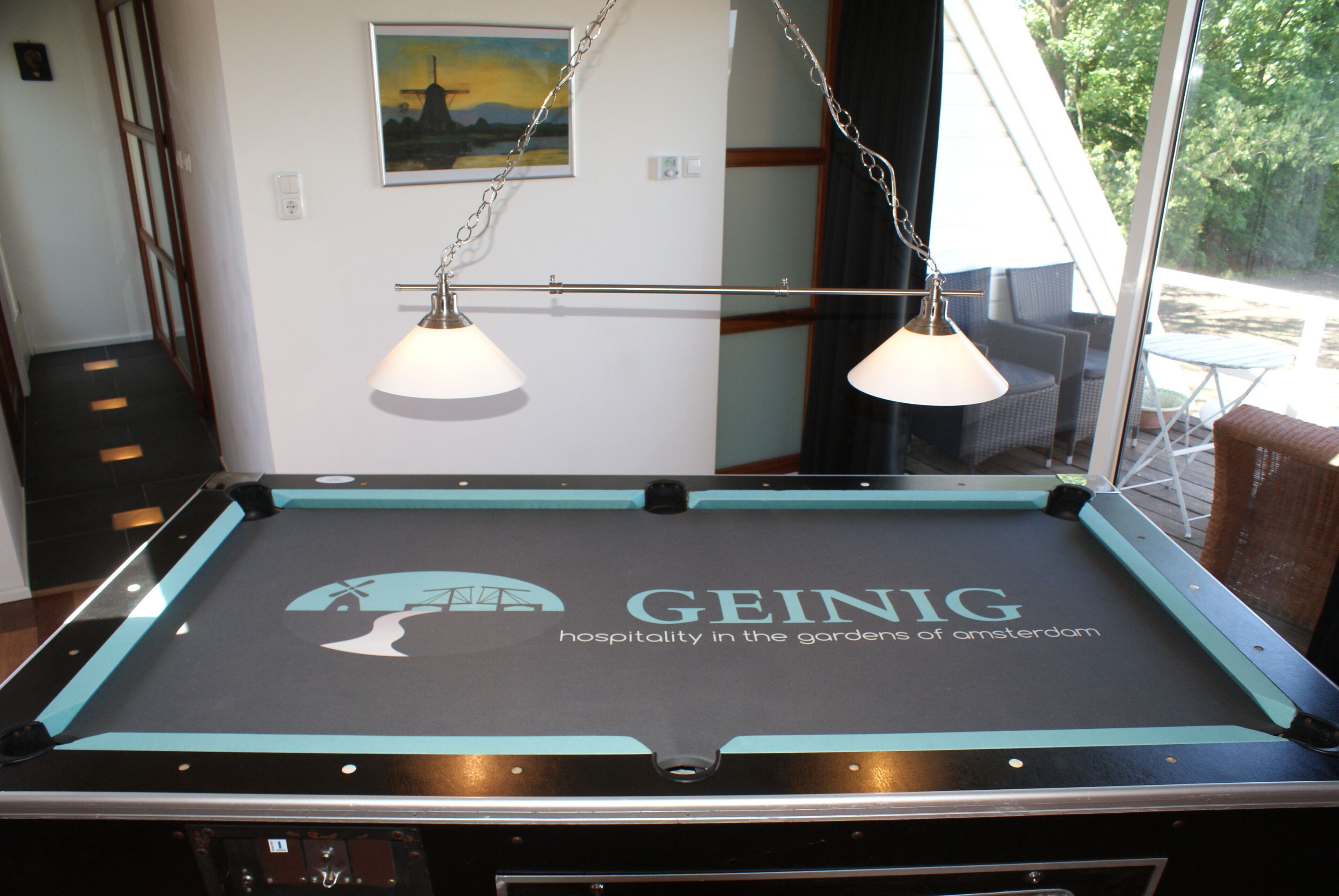 A pool table with a GEING logo and a view of the outdoors through a window.