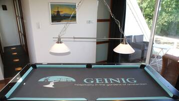 A pool table with a GEING logo and a view of the outdoors through a window.