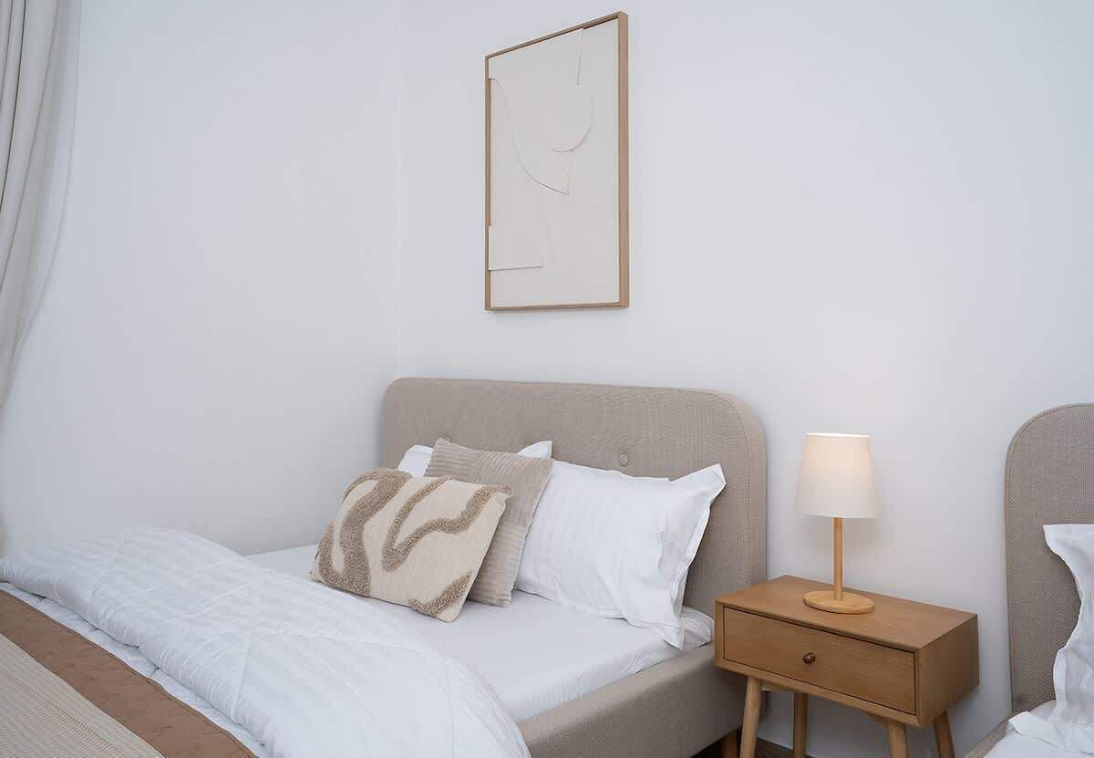 A bedroom with a bed, pillows, a nightstand with a lamp, and a wall-mounted artwork.