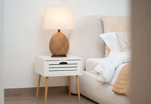 A white bedside table with a lamp and a drawer, next to a bed with a beige blanket. - Beachfront Apartment W Pool & Balcony Cyan Beach (Sharjah)