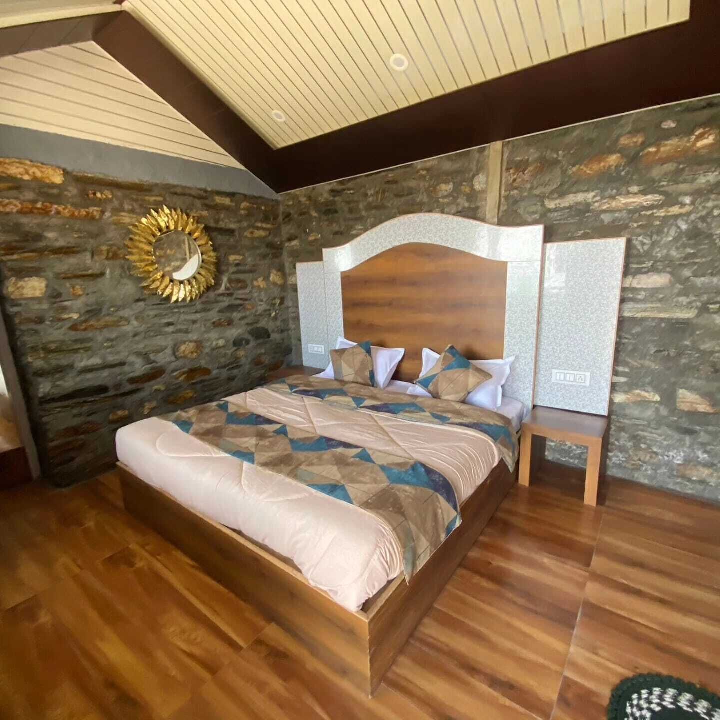 A bedroom with a stone wall, wooden headboard, and a bed with patterned bedding.