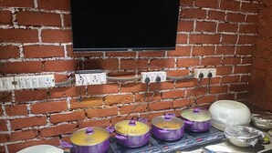 Ein reichhaltiges Buffet mit mehreren violetten Töpfen auf einer Tischplatte, ein Flachbildfernseher an einer Ziegelwand und verschiedene Geschirrteile sowie Besteck.