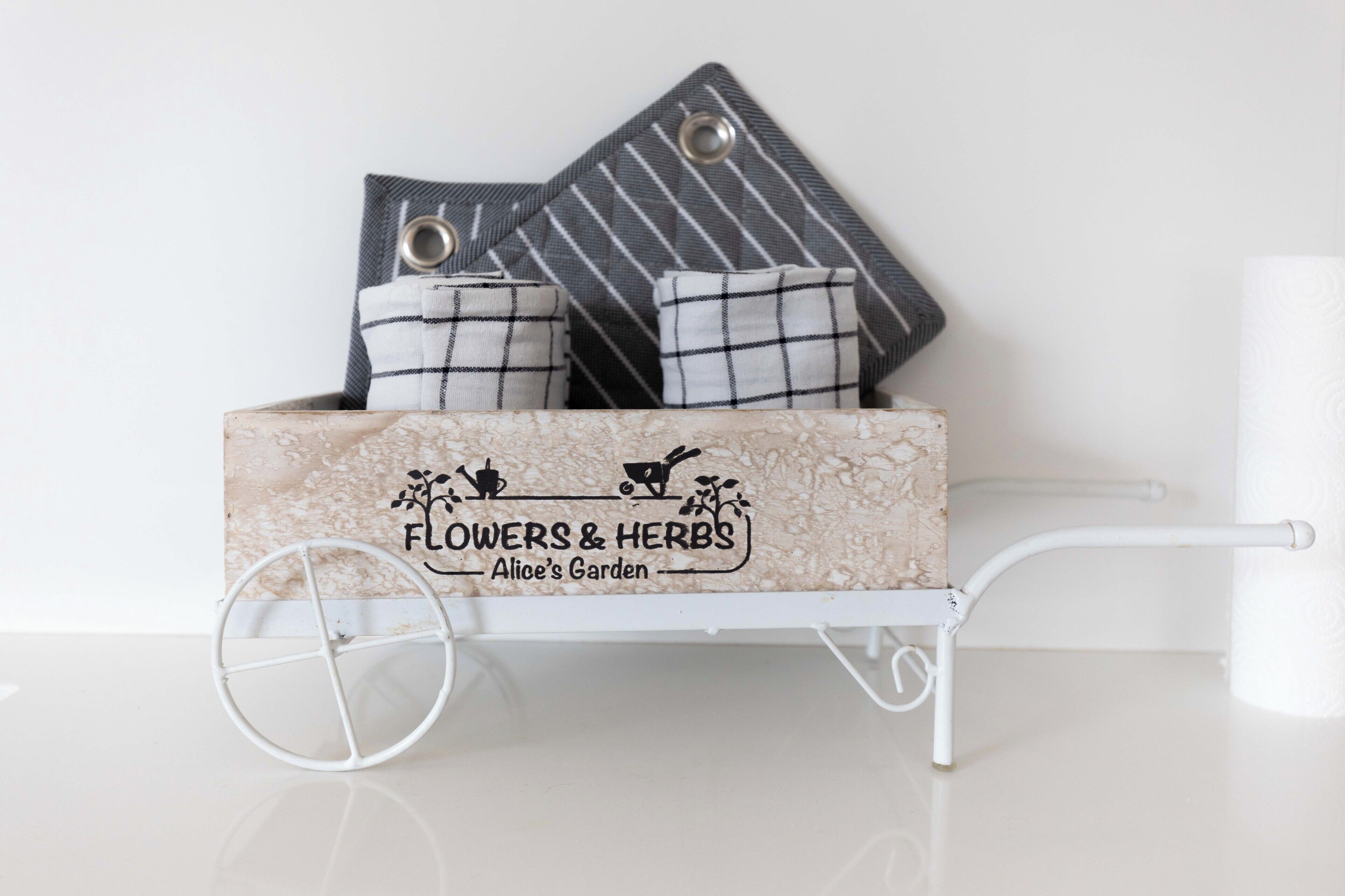 A white metal cart with a floral and herb-themed box labeled "Flowers & Herbs" and "Alice's Garden."