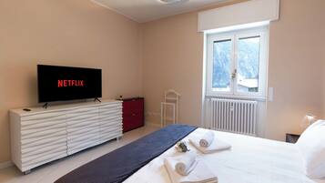 A hotel room with a bed, a TV on a white dresser, a window with a view, and a radiator.