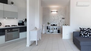 A modern kitchen with a built-in oven, a white dining area with a sofa, and a marble wall with a light fixture. - TERRACE ON LAKE ⭐️ ⭐️⭐️⭐️⭐️ Open Space & Netflix [Free Parking Area] (Lecco)