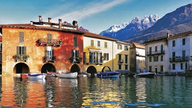A canal with buildings on one side and mountains in the background. - TERRACE ON LAKE ⭐️ ⭐️⭐️⭐️⭐️ Open Space & Netflix [Free Parking Area] (Lecco)