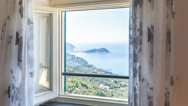 Una ventana con vista a un paisaje costero, que incluye una masa de agua y una isla distante.