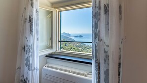 Una habitación con ventana que da a un paisaje costero, aire acondicionado integrado y una puerta con cortina floral.