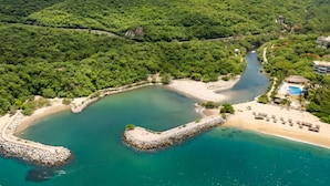 Vista aérea de uma área costeira com uma baía curva, uma praia de areia e uma pequena ilha rochosa.