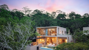 Uma casa moderna de dois andares com piscina, rodeada por uma floresta densa.