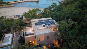 Uma propriedade costeira com painel solar no terraço, praia e um farol ao fundo.