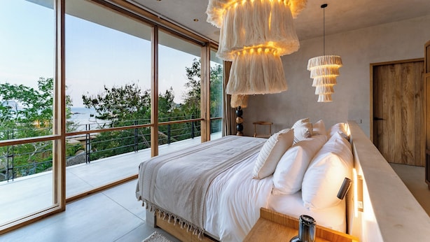 Quarto moderno com cama grande, vista para o verde e varanda, e luminária pendente de design exclusivo.
