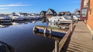 Un puerto deportivo con varias embarcaciones amarradas, un muelle de madera y una hilera de casas al fondo.