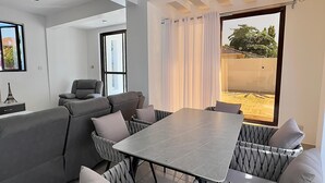 Een moderne woonkamer met een grijze bank, een eettafel en een stoelopstelling met een patroon.