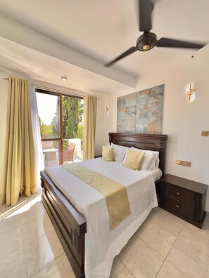 A bedroom with a large bed, a ceiling fan, a nightstand, and a view through a sliding glass door to the outdoors. - Elkhart Fereinhaus Villa (Mombasa)