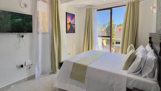 Een hotelkamer met een bed, een plafondventilator, een televisie en een raam met gordijnen.