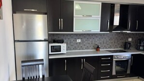A modern kitchen with dark cabinets, a stainless steel refrigerator, a microwave, and a dining table with chairs. - Villa Bushi (Ksamil)