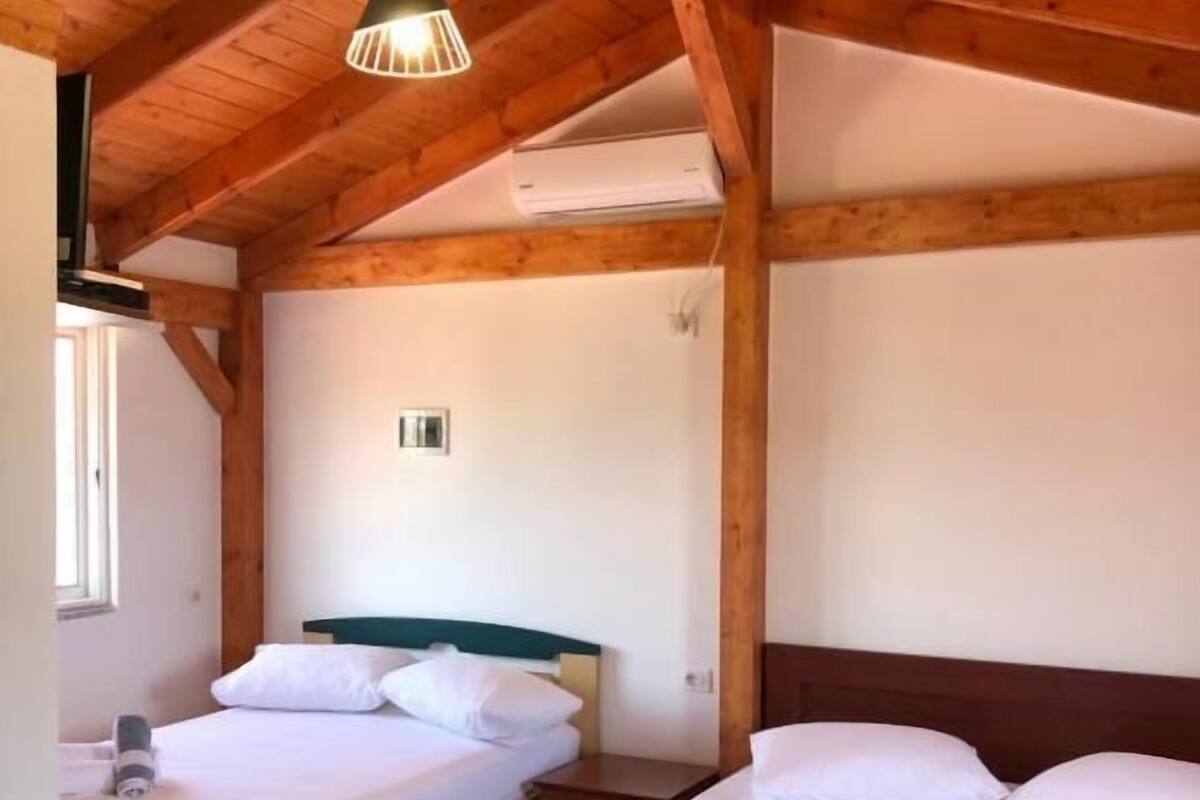 A room with two beds, wooden beams, a hanging light fixture, and an air conditioning unit.