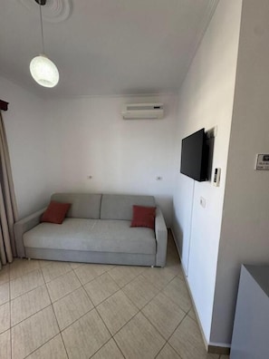 A living room with a sofa, a flat-screen TV mounted on the wall, and an air conditioning unit. - Villa Bushi (Ksamil)