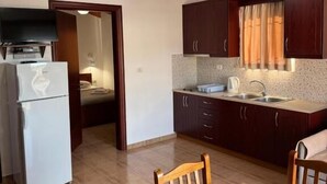 A compact kitchen with wooden beams, a refrigerator, a sink, and a dining area with a table and chairs. - Villa Bushi (Ksamil)