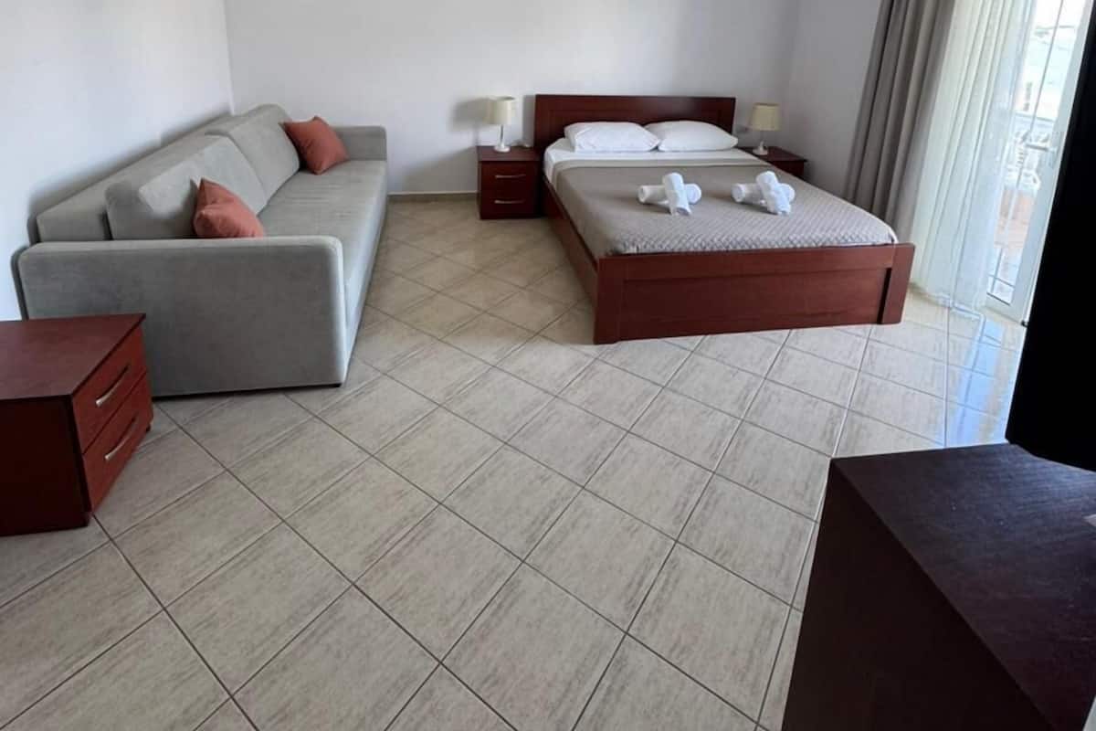 A hotel room with a bed, a sofa, a bedside table, a lamp, and a ceiling light.