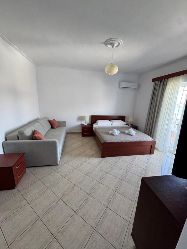 A hotel room with a bed, a sofa, a bedside table, a lamp, and a ceiling light.