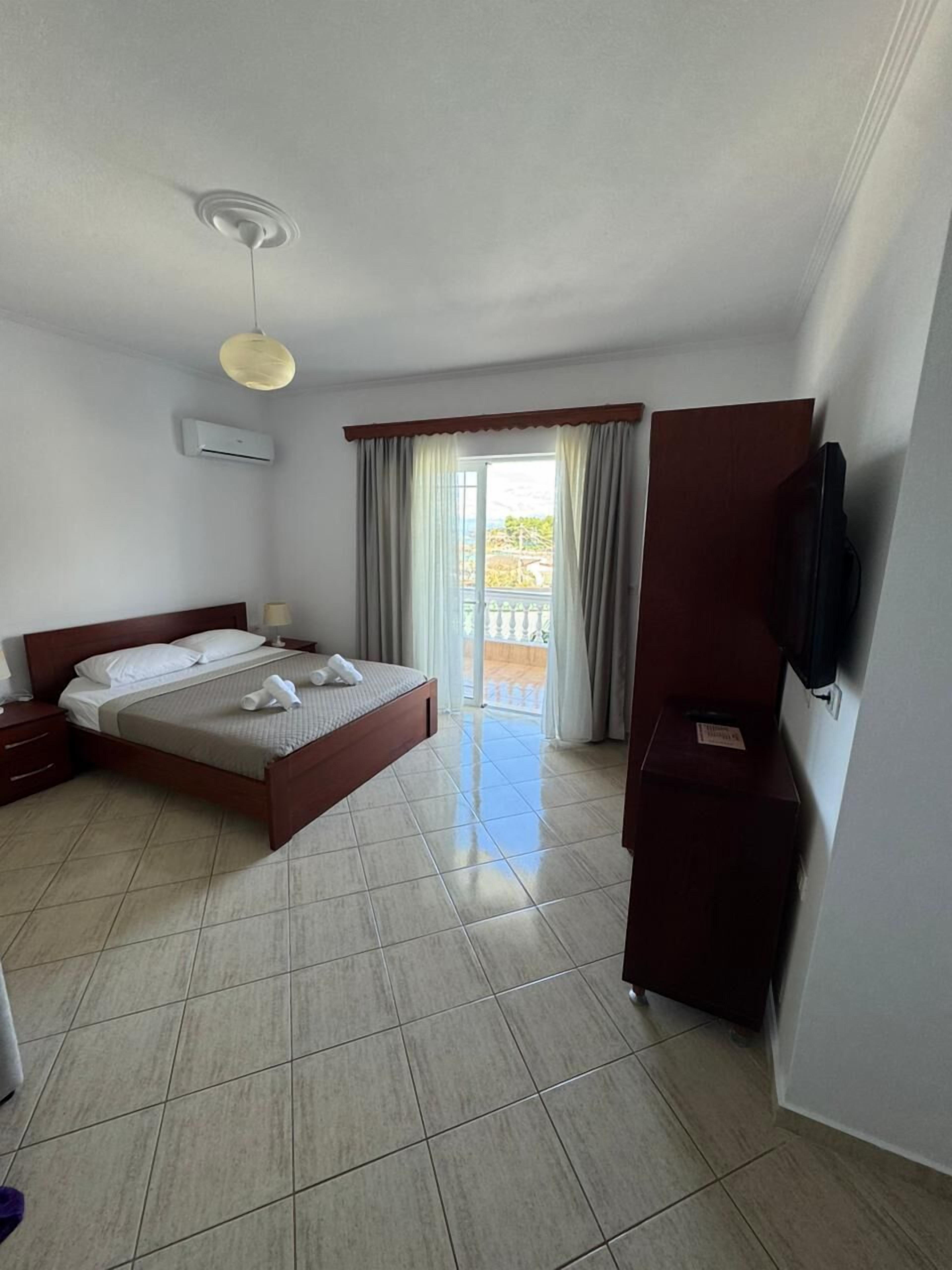 Una habitación de hotel con cama, televisor, armario y balcón con cortinas.