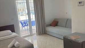 A hotel room with a bed, a sofa, a chair, a small refrigerator, and a view of the outside. - Villa Bushi (Ksamil)
