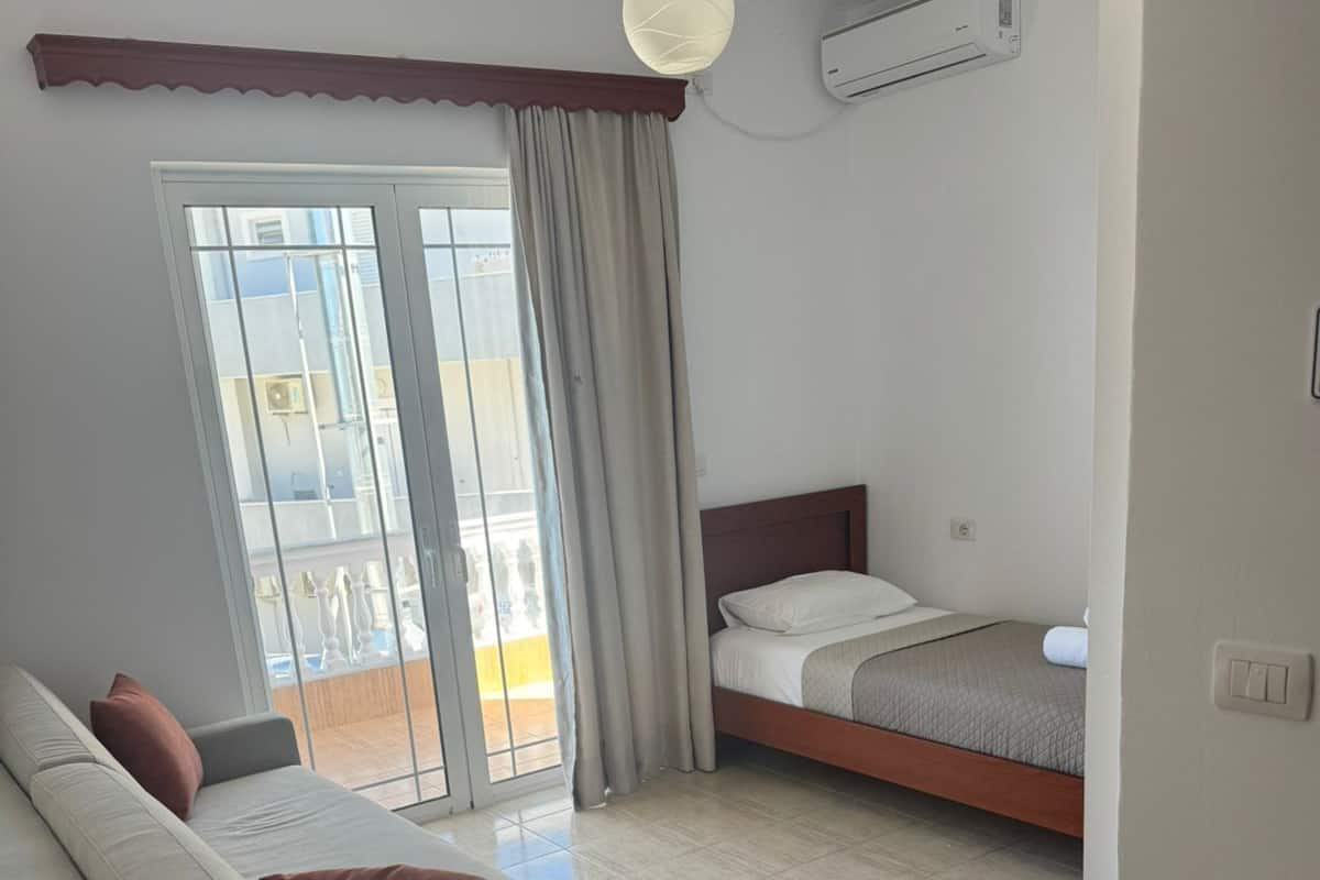 A modern hotel room with a sofa, a bed, a balcony, and an air conditioning unit.