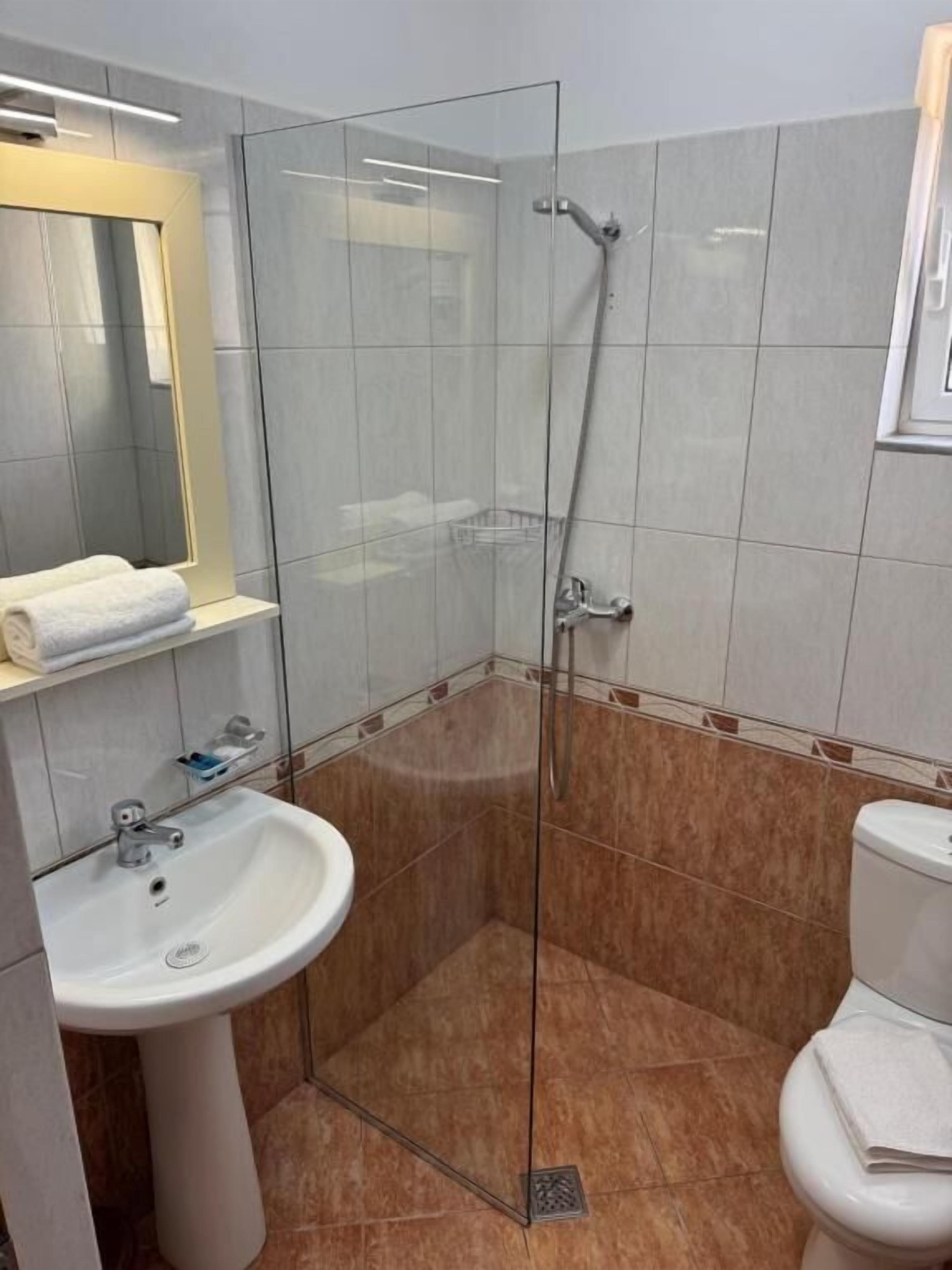 A modern bathroom with a glass shower enclosure, a pedestal sink, and a toilet.