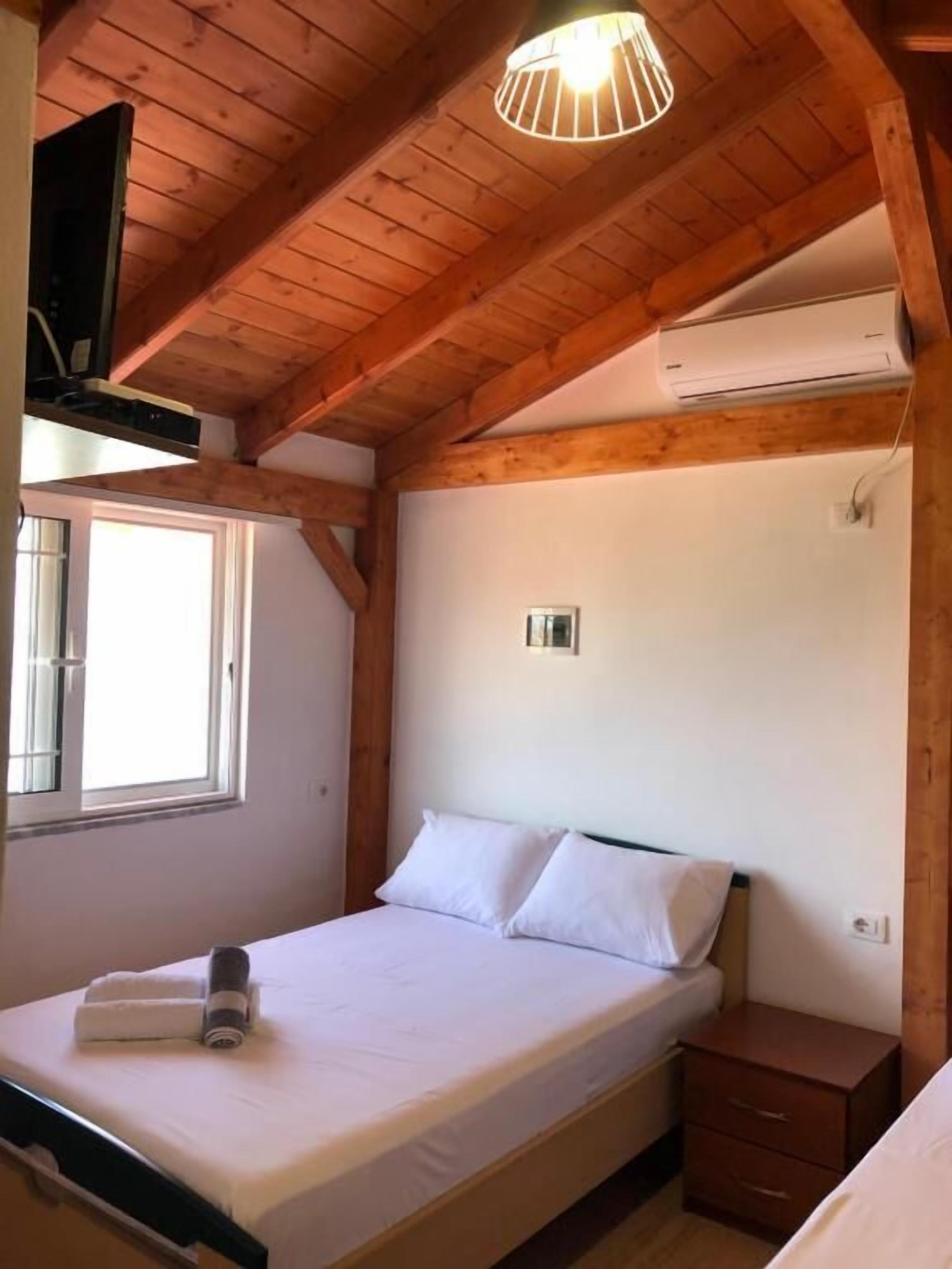 A bedroom with a wooden ceiling, a bed with white linens, a bedside table, and an air conditioning unit.