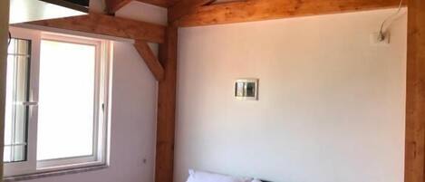 A bedroom with a wooden ceiling, a bed with white linens, a bedside table, and an air conditioning unit.