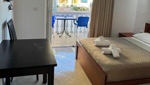 A hotel room with a bed, a desk, a chair, a TV, and a balcony with a table and chairs. - Villa Bushi (Ksamil)