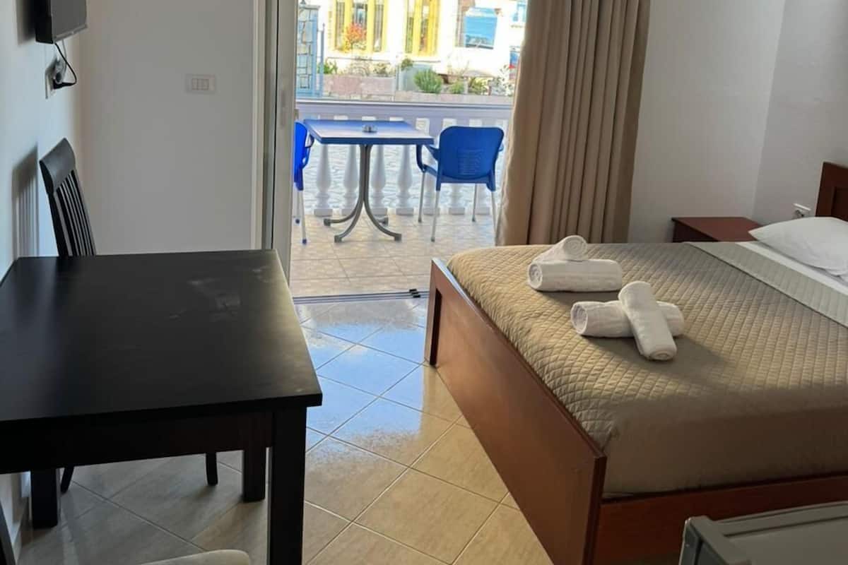 A hotel room with a bed, a desk, a chair, a TV, and a balcony with a table and chairs.
